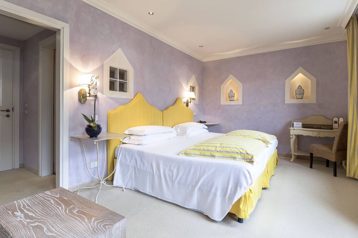Una habitación de hotel con cama, mesita de noche, lámpara y apliques decorativos.