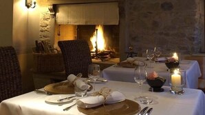 A dining area with a fireplace, wicker chairs, and tables set for two with wine glasses and candles. - Hotel Dei Chiostri (Follina)