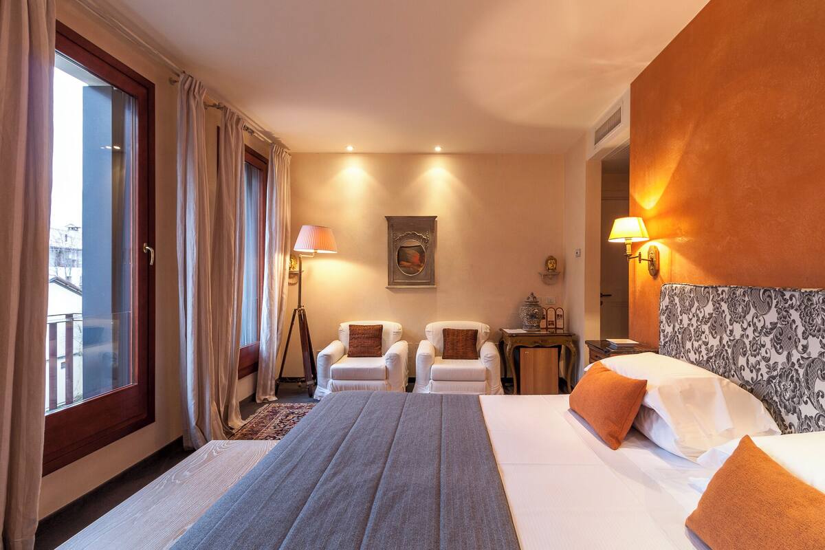 Habitación de hotel con una cama grande, dos sillones, una lámpara de pie y un cuadro en la pared.