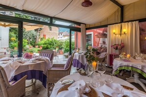 An outdoor dining area with tables set for a meal, surrounded by wicker chairs and covered by a canopy.