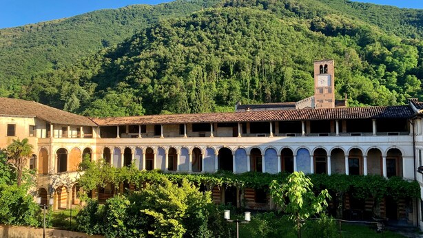 A historic building with a central courtyard, a bell tower, and a mountainous backdrop. - Hotel Dei Chiostri (Follina)