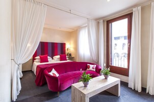 A hotel room with a bed, a red sofa, a wooden coffee table, and a view of the outside.