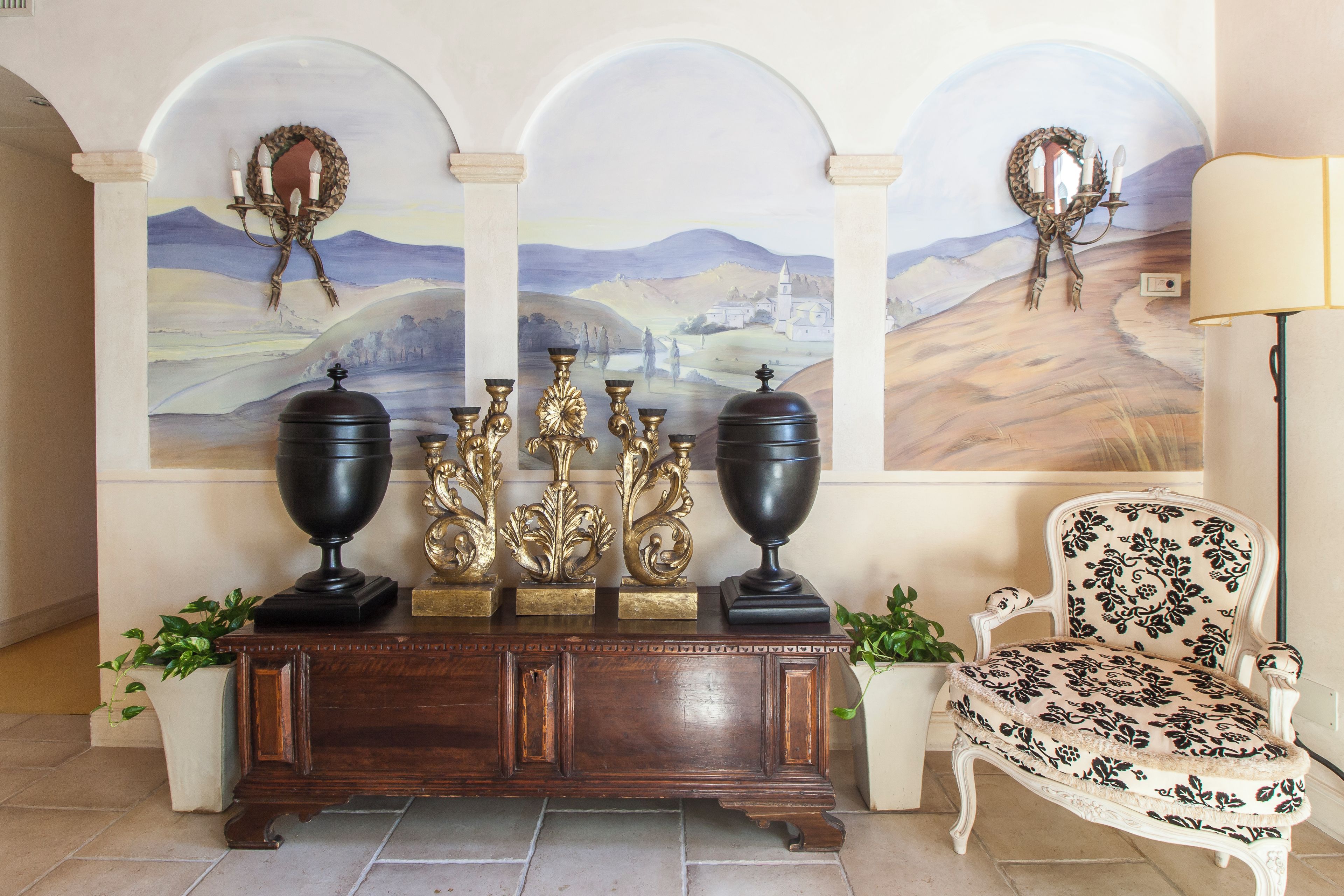 A lobby with a wooden console table, three paintings, a chair, and a lamp.