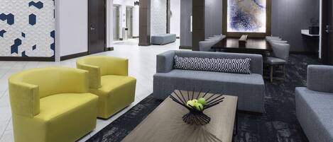 A modern lobby with a seating area, a coffee table with a fruit centerpiece, and a large abstract wall art piece.