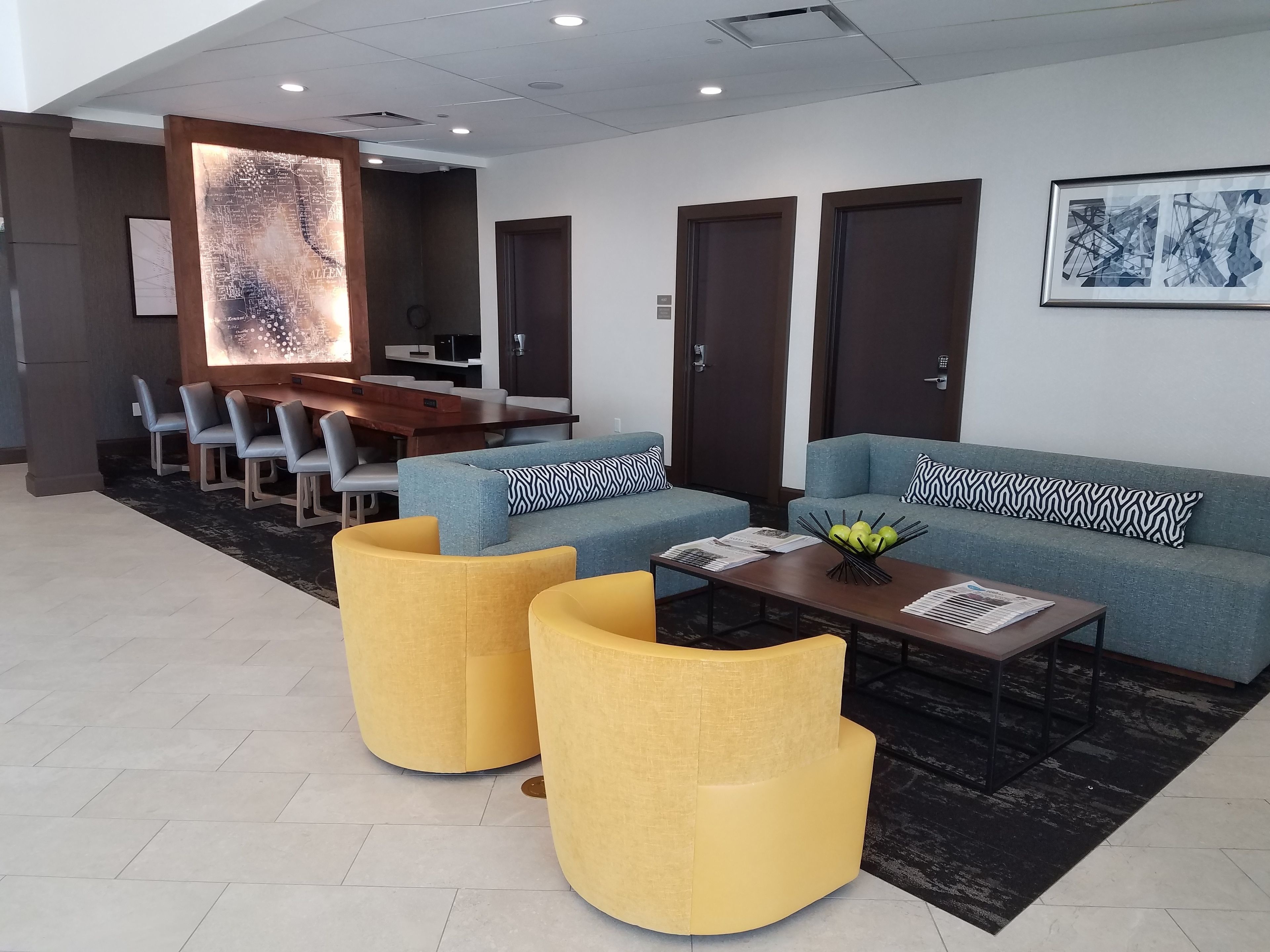 Un vestíbulo moderno con una zona de estar que incluye sofás y sillones, un mostrador de recepción de madera, y un área de comedor con sillas y una mesa.