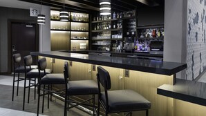 A bar area with a long counter, multiple bar stools, and shelves stocked with bottles and glasses.