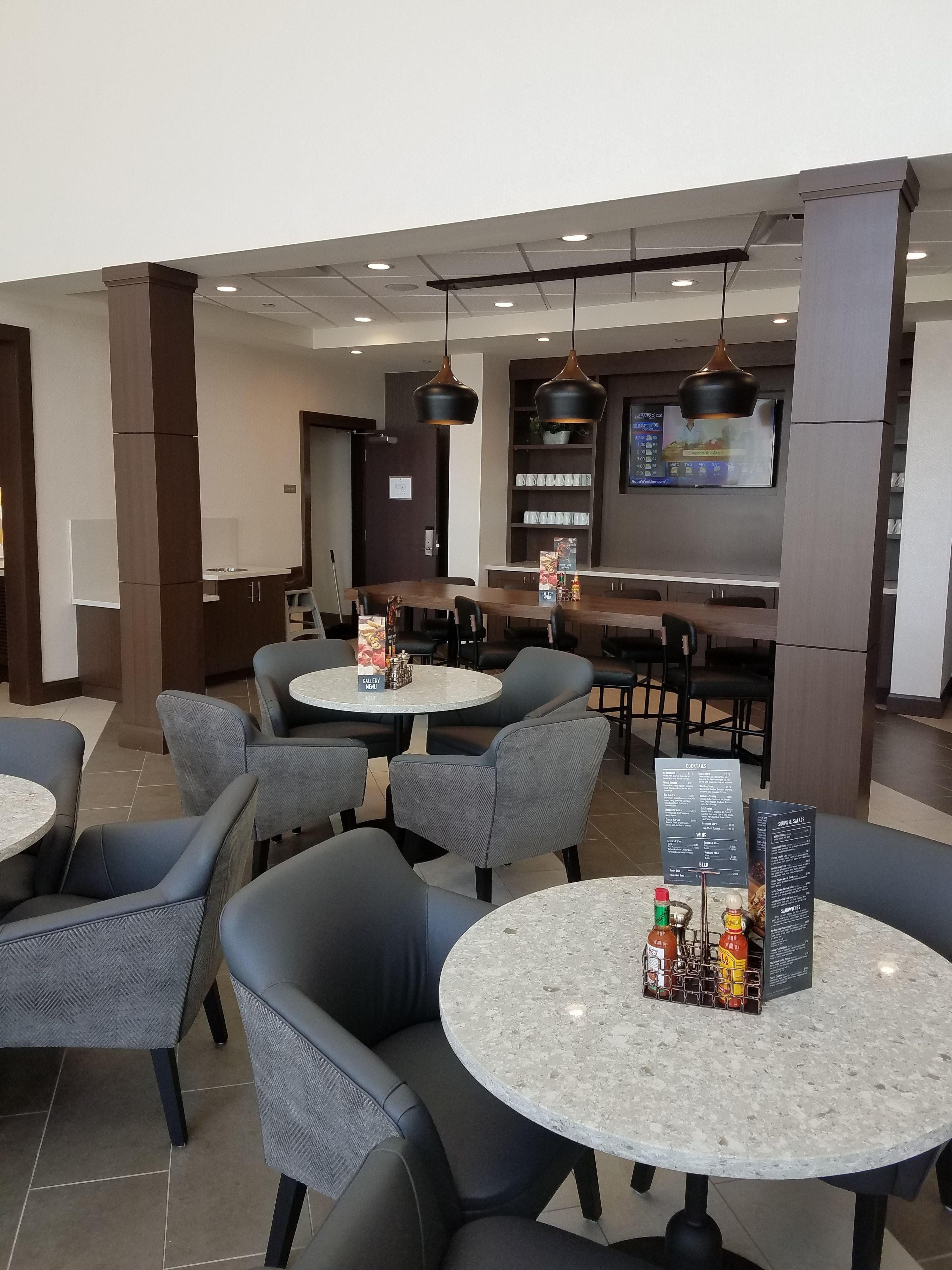 A modern restaurant with round tables and chairs, a menu board, and a TV displaying a menu.