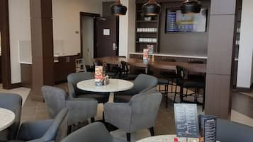 A modern restaurant with round tables and chairs, a menu board, and a TV displaying a menu.