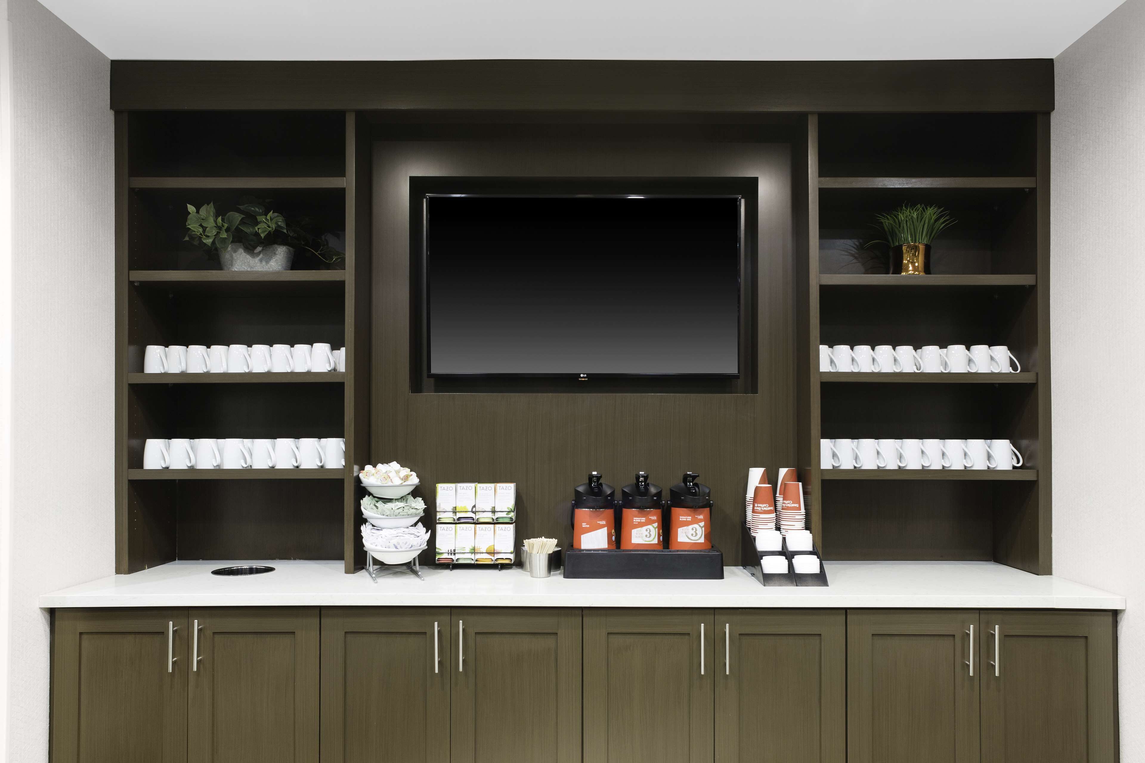 A modern kitchen with a built-in TV, shelves with kitchenware, and a coffee station.