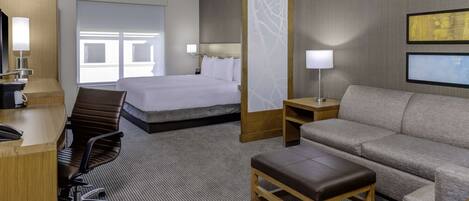 A hotel room with a bed, a sofa, a desk, and a chair.