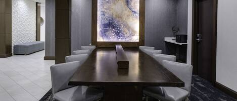 A conference room with a long table, white chairs, a large abstract wall art piece, and a carpeted floor.