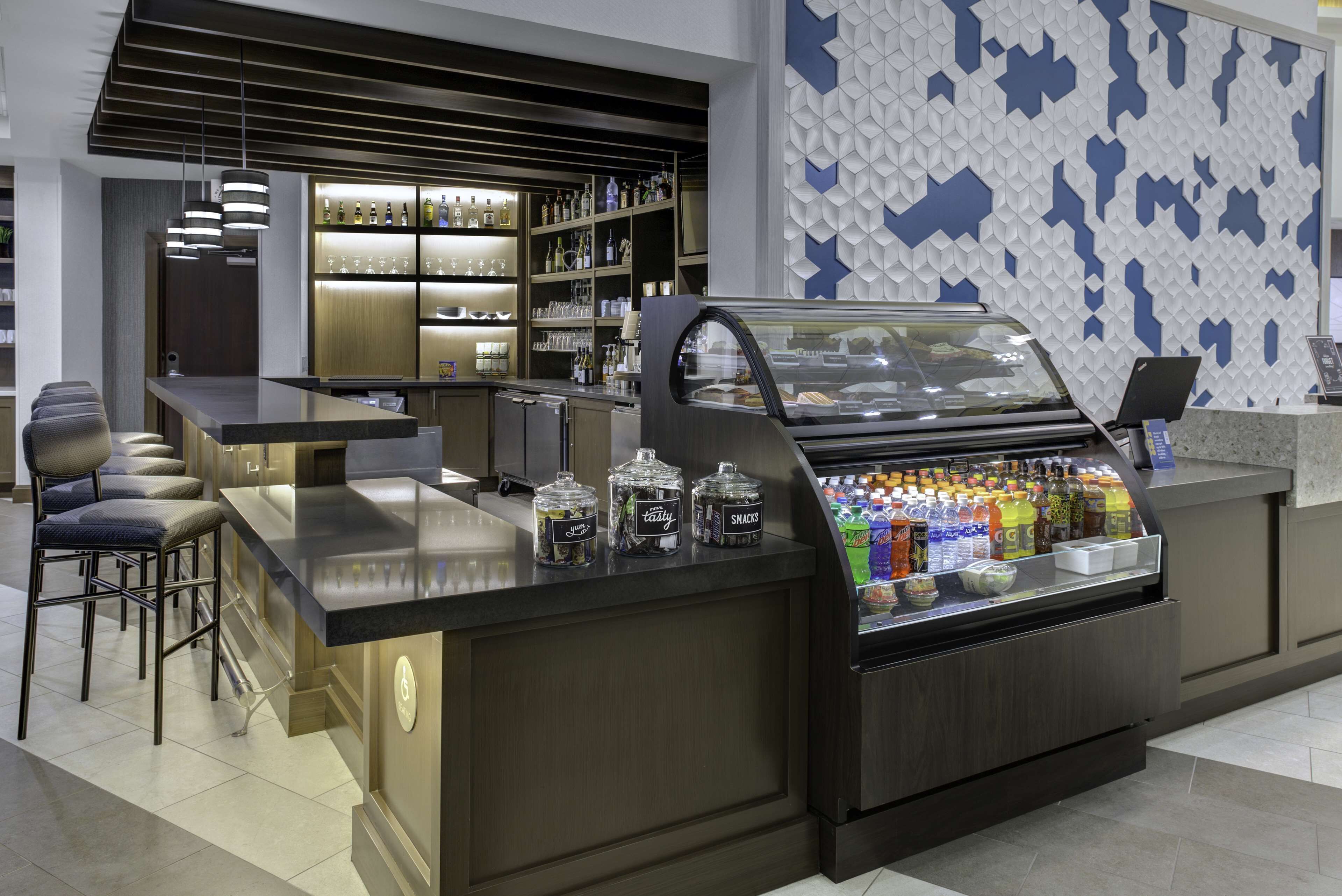 Zona de bar moderna con barra, asientos y un expositor con aperitivos y bebidas.