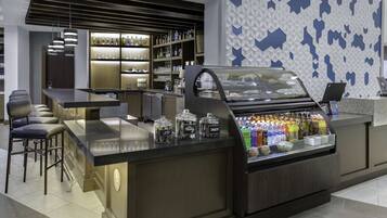 Zona de bar moderna con barra, asientos y un expositor con aperitivos y bebidas.