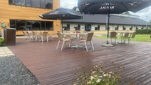 An outdoor patio area with wooden flooring, outdoor seating with wicker chairs and tables, and two umbrellas with the "ROYAL" logo. - Danhostel Thorhallen Jels (Rodding)