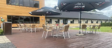 An outdoor patio area with wooden flooring, outdoor seating with wicker chairs and tables, and two umbrellas with the "ROYAL" logo.