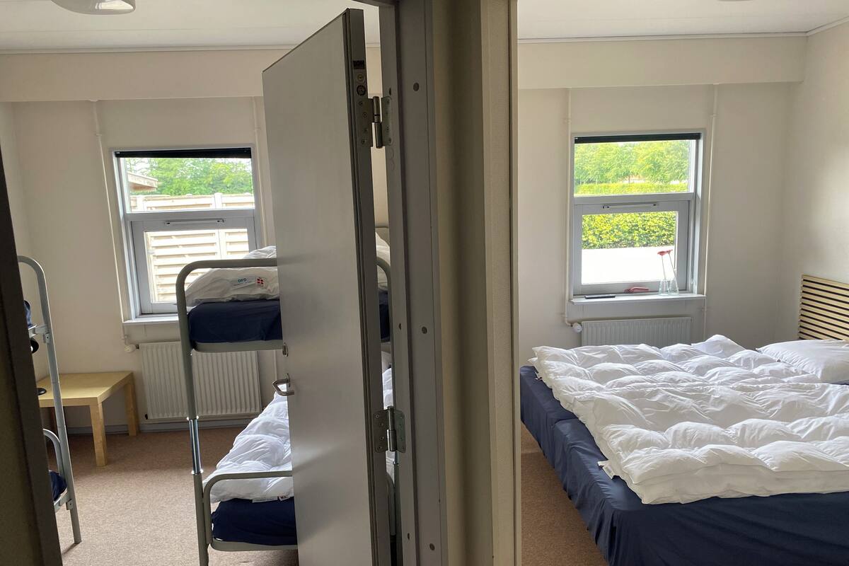 Ein Schlafzimmer mit Etagenbett, Nachttisch, Fenster mit Blick auf Grünflächen und Heizkörper.