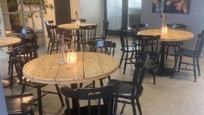A modern dining area with round wooden tables and black chairs, featuring a large painting on the wall. - Danhostel Thorhallen Jels (Rodding)
