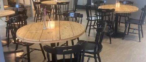 A modern dining area with round wooden tables and black chairs, featuring a large painting on the wall.