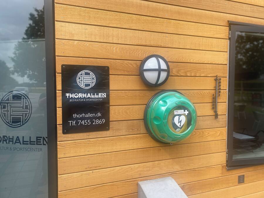 Pared de madera con un letrero del Centro Cultural y Deportivo Thorhallen Jels, un buzón y un buzón verde con un símbolo de corazón.