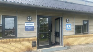 A building with a metal roof, a door with a glass panel, and two signs on the wall. - Danhostel Thorhallen Jels (Rodding)