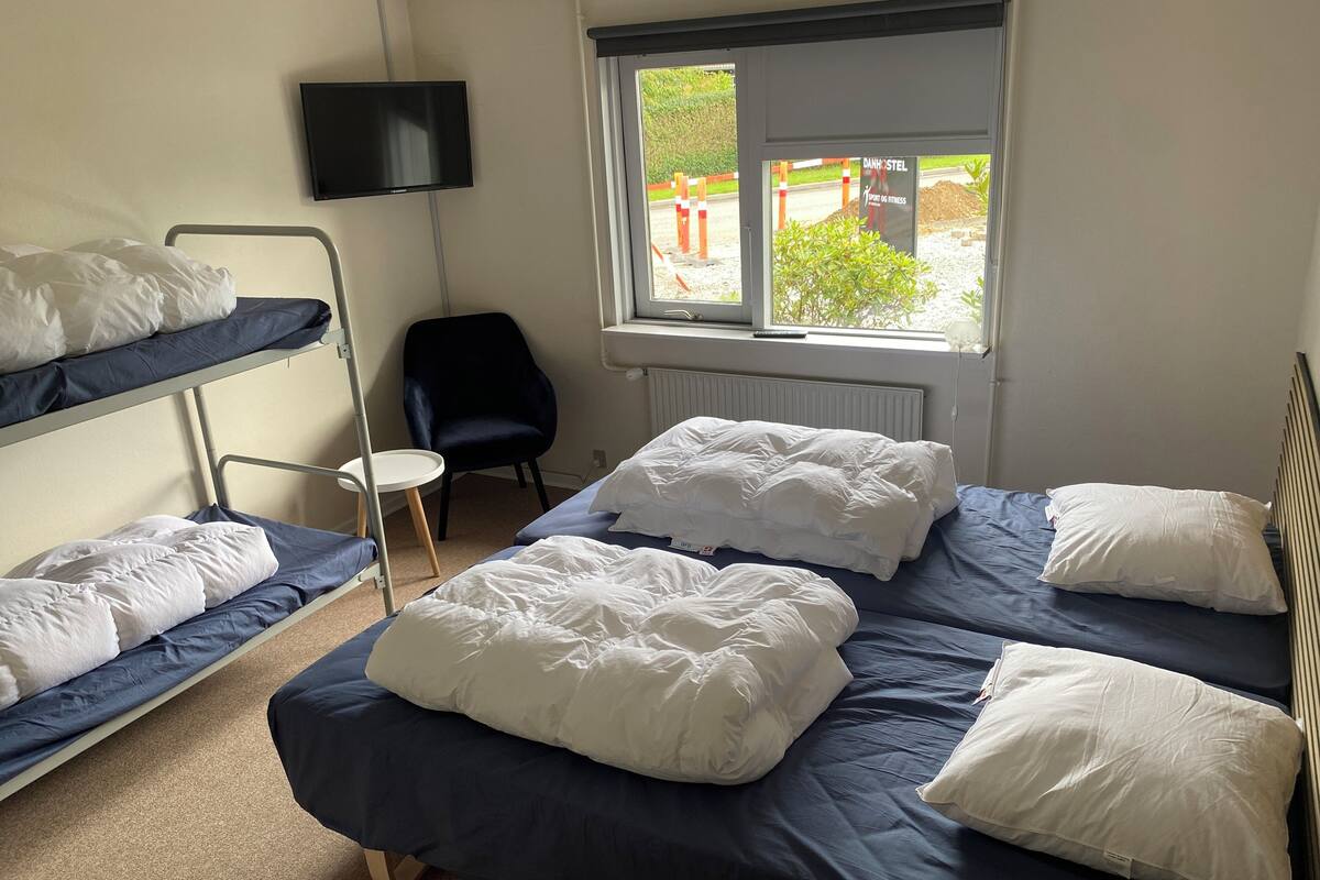 Ein Schlafsaalzimmer mit Etagenbetten, einem Schreibtisch, einem Stuhl und einem Fenster mit Blick nach draußen.