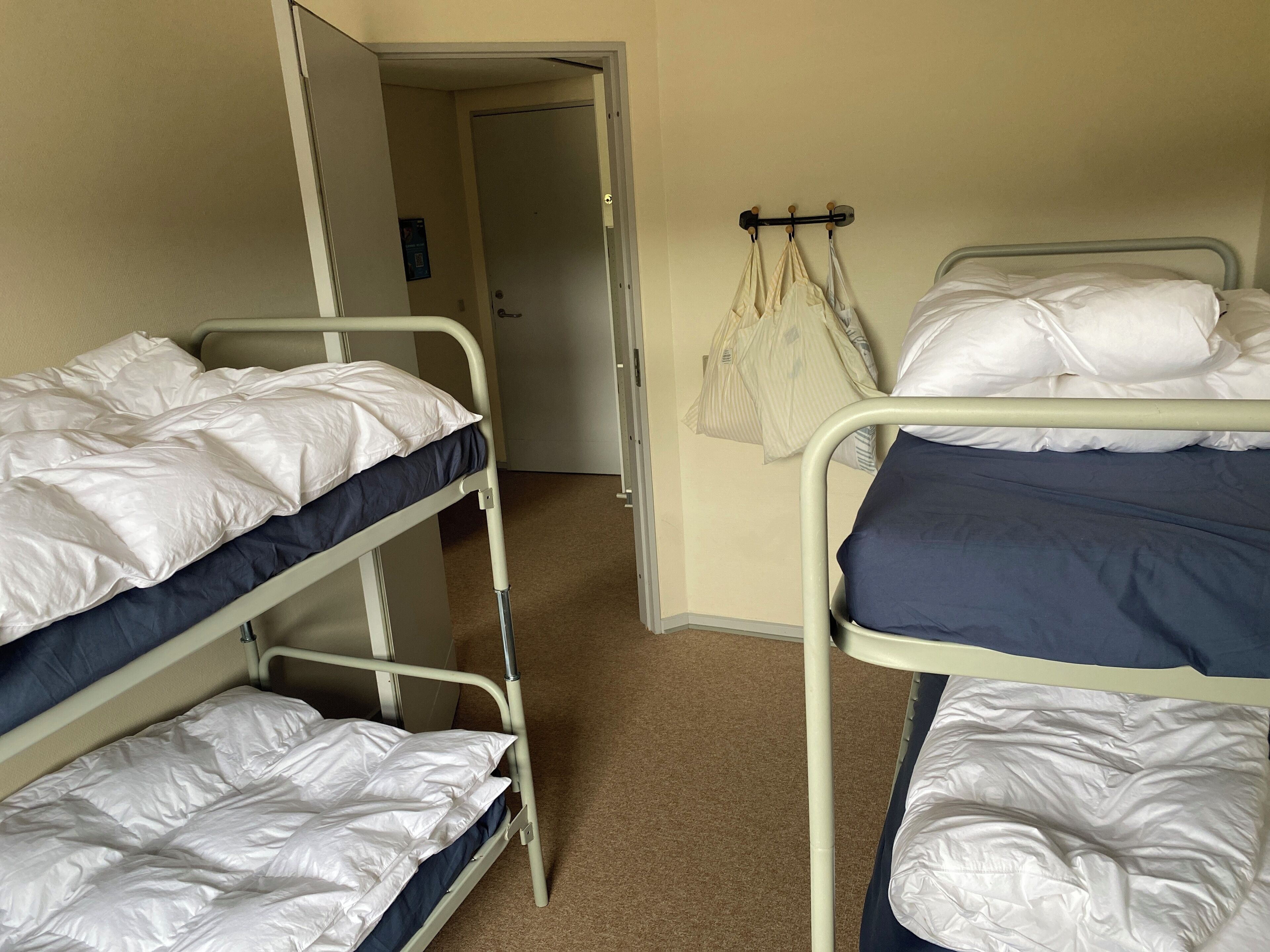 A dormitory room with bunk beds, a door, and a coat rack with bags.