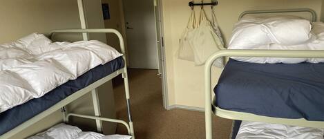 A dormitory room with bunk beds, a door, and a coat rack with bags.