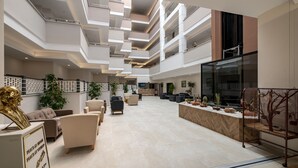 Un vestíbulo amplio con varias zonas de estar, una recepción y un diseño arquitectónico moderno con techo alto y varios niveles.