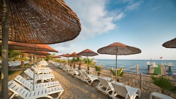 Un área de descanso junto a la playa con sillas blancas y sombrillas de paja, con vista al mar.