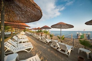 A beachside lounge area with white lounge chairs and thatched umbrellas, overlooking the sea. - Club Dizalya Hotel (Alanya)