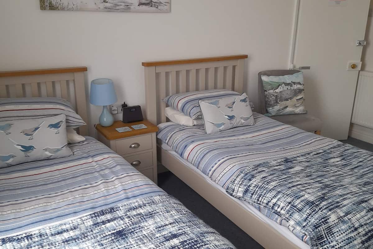 A bedroom with two beds, a bedside table with a lamp, a painting on the wall, and a door with a fire action sign.