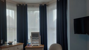 A hotel room with a desk, chair, dresser, and a TV on the wall. - South Rising Guest House (Poole)