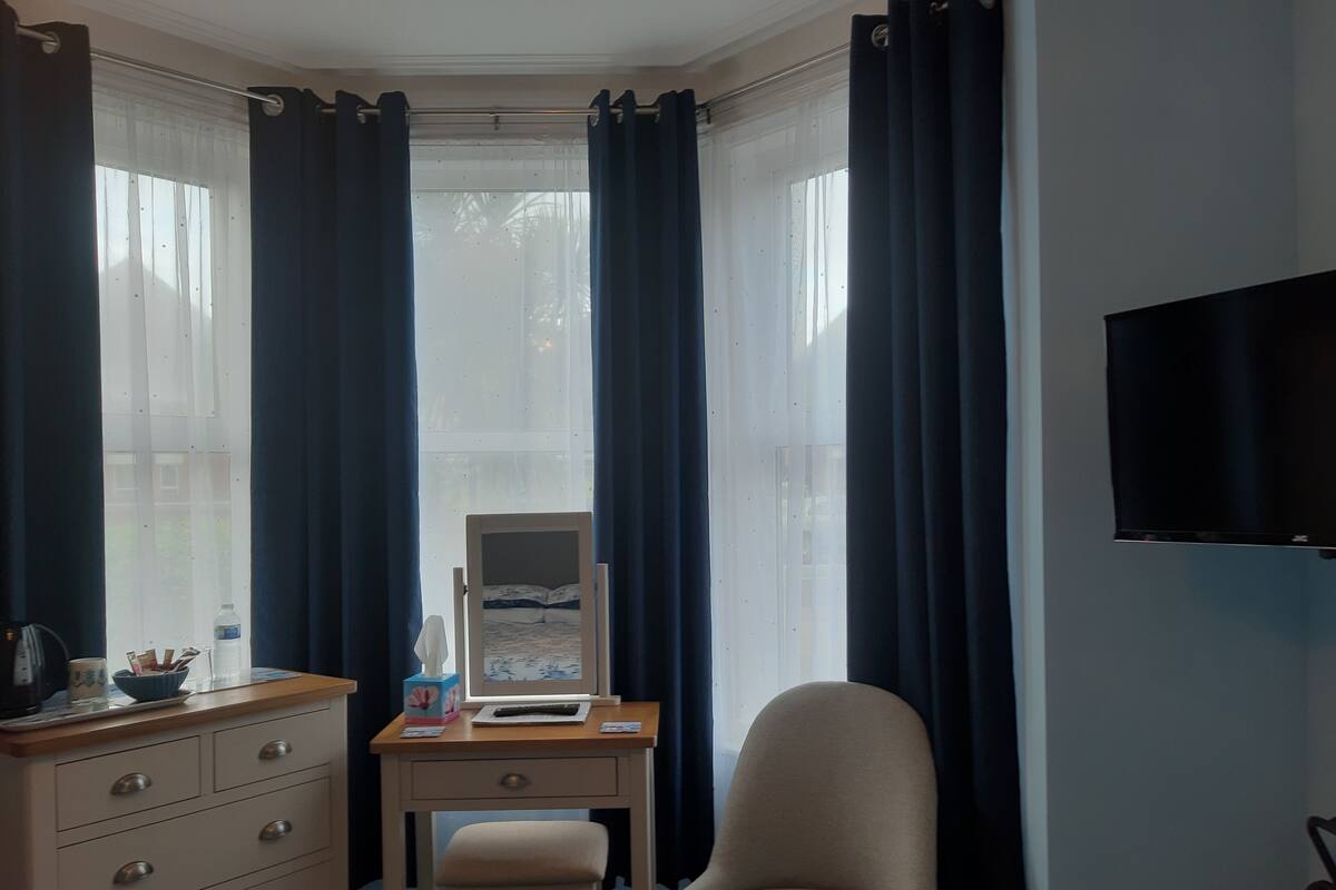 A hotel room with a desk, chair, dresser, and a TV on the wall.