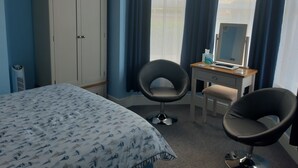 A hotel room with a bed, two chairs, a desk with a computer, a mirror, and a wardrobe. - South Rising Guest House (Poole)