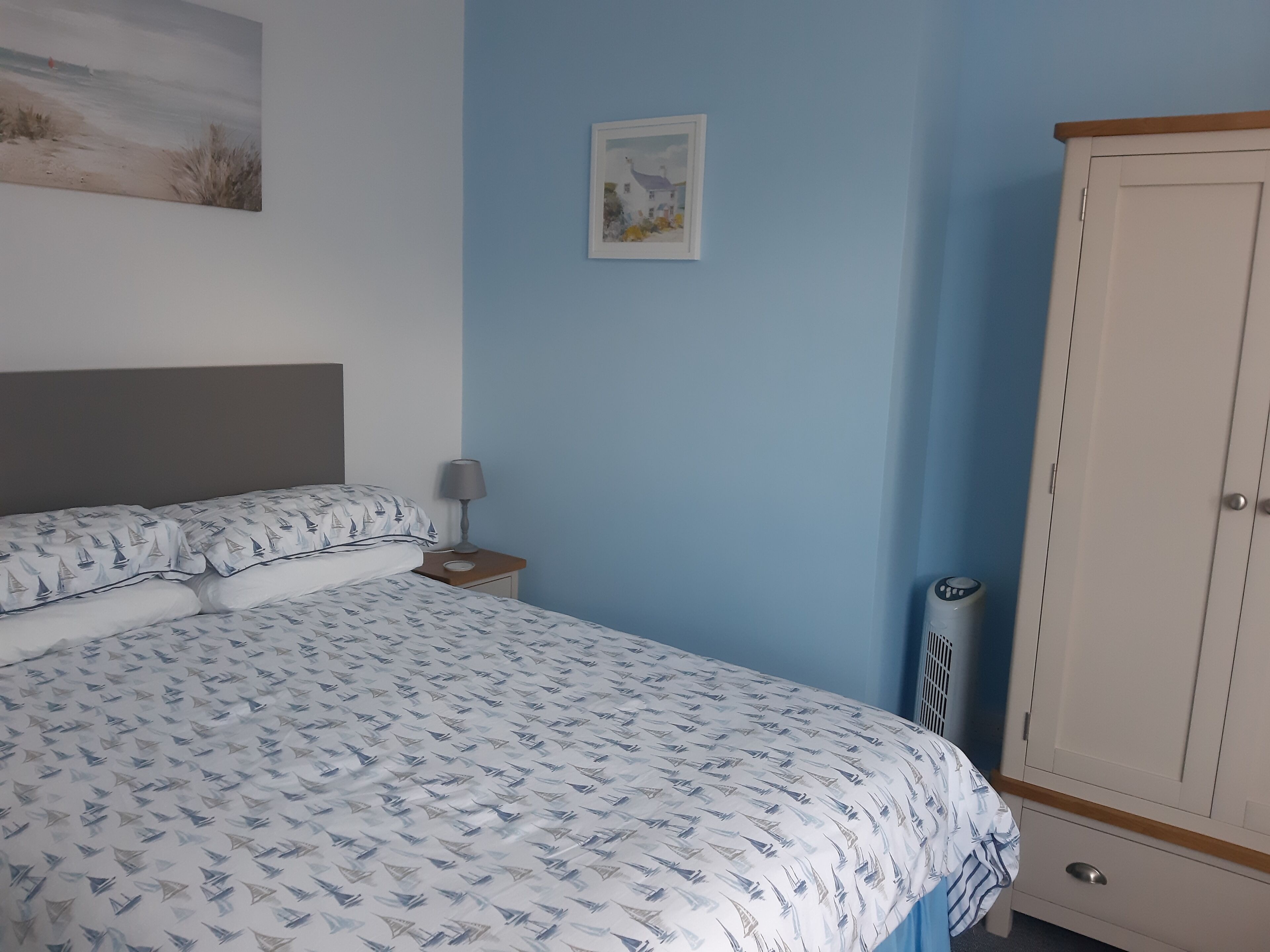 Une chambre à coucher comprenant un lit, une table de chevet, une armoire et un mur orné d’un tableau.