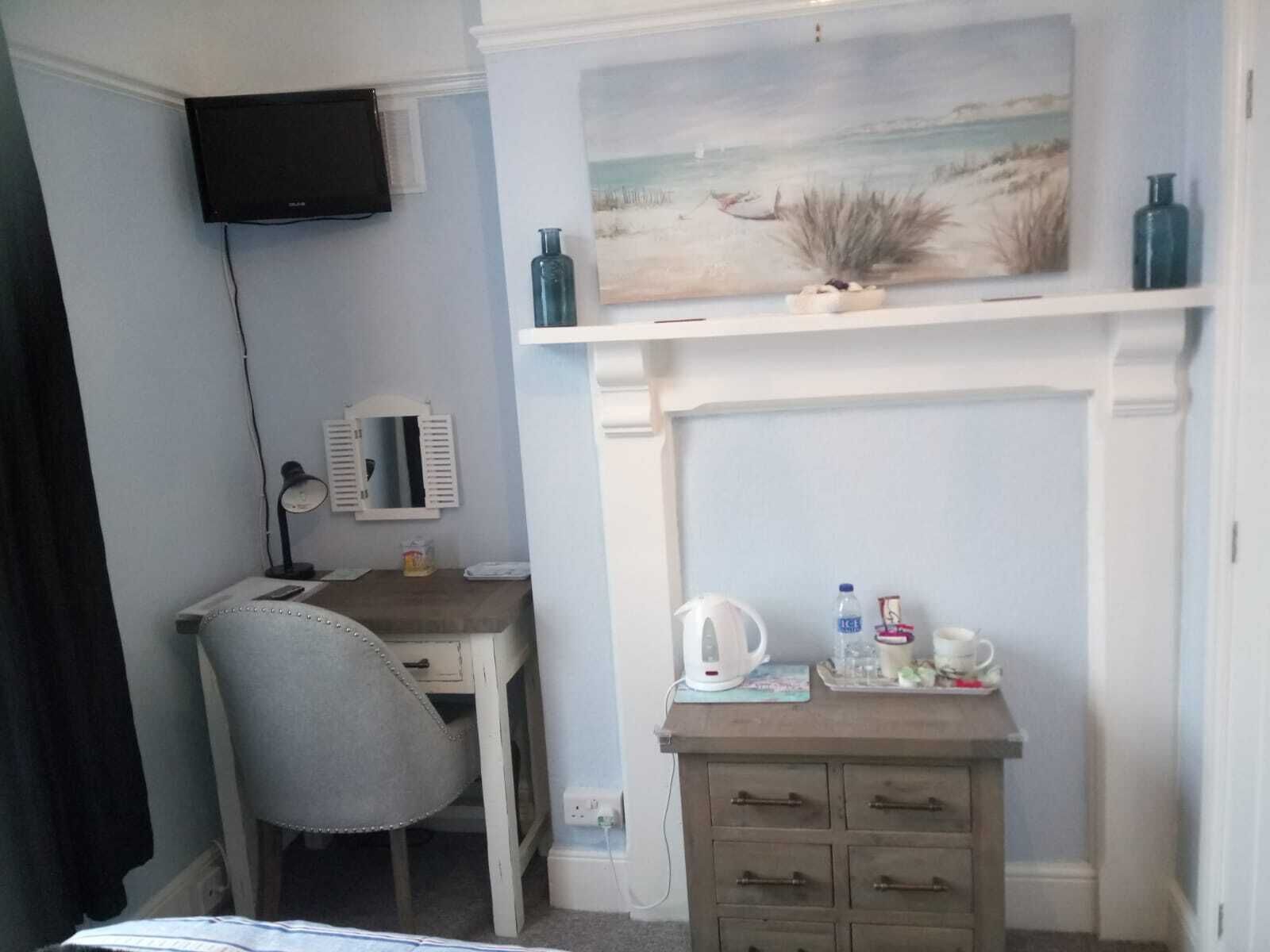 A bedroom with a desk, chair, and a painting of a beach scene.