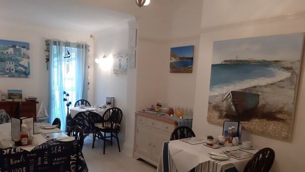 A dining area with a table set for two, a cabinet, and artwork on the walls. - South Rising Guest House (Poole)