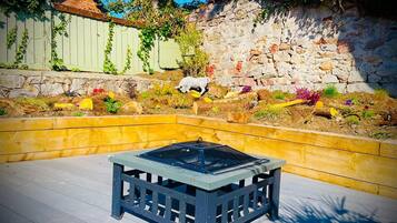 Une terrasse avec une table carrée, entourée de jardinières surélevées où sont plantées différentes espèces de plantes et de fleurs.