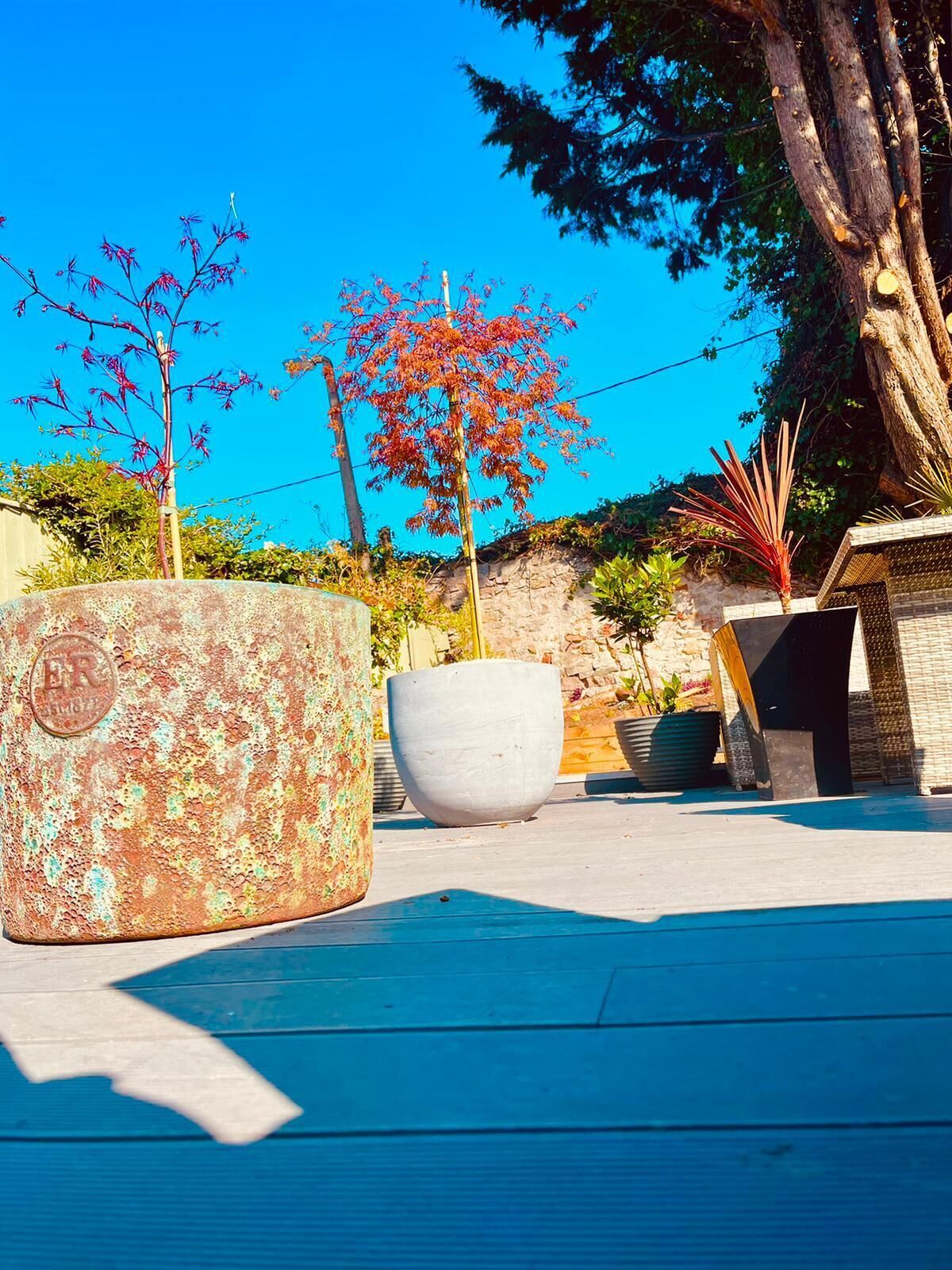 A blue wooden deck with large planters and a tree with red leaves.