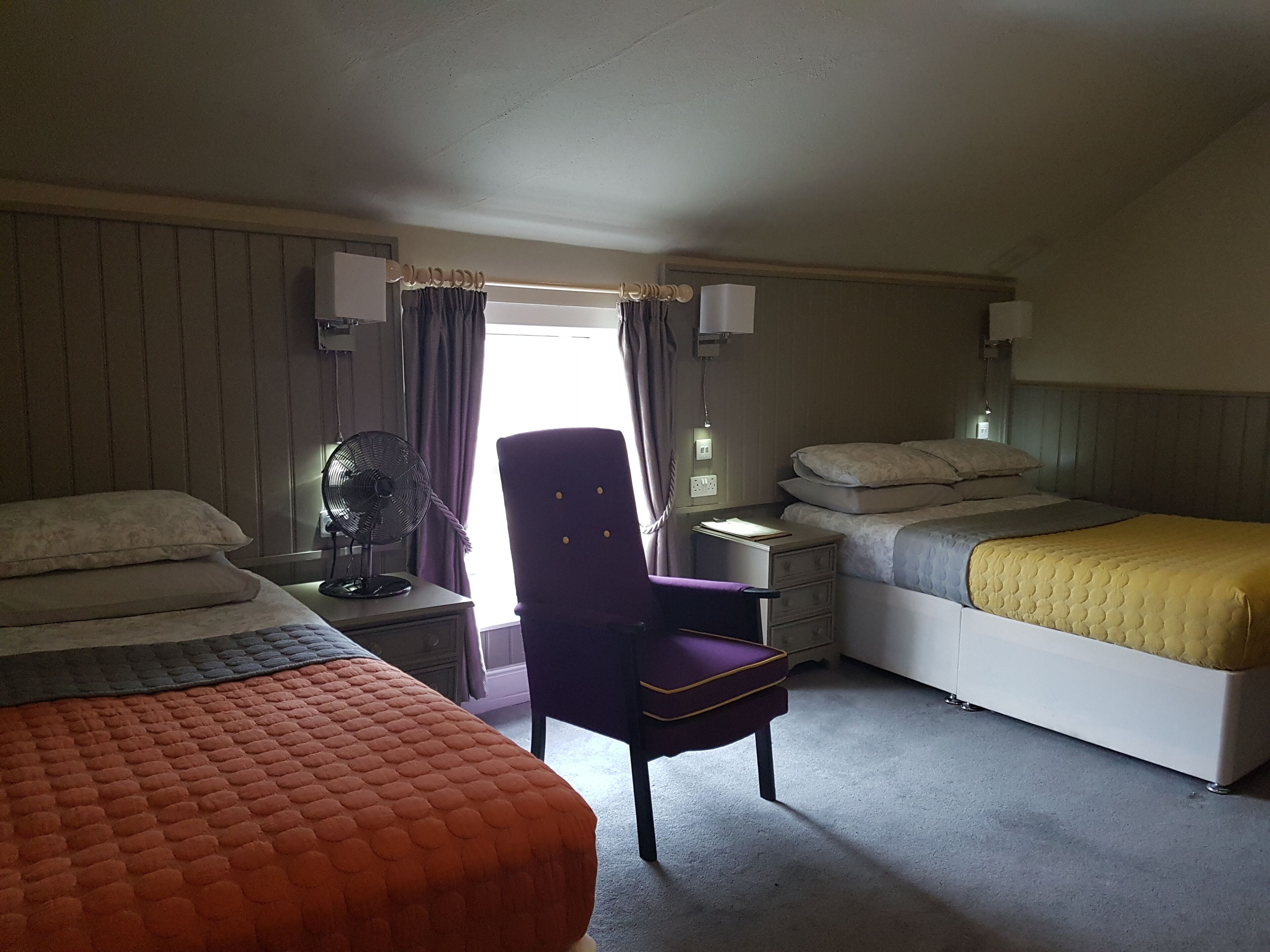 A hotel room with two beds, a chair, a desk, and a window with curtains.