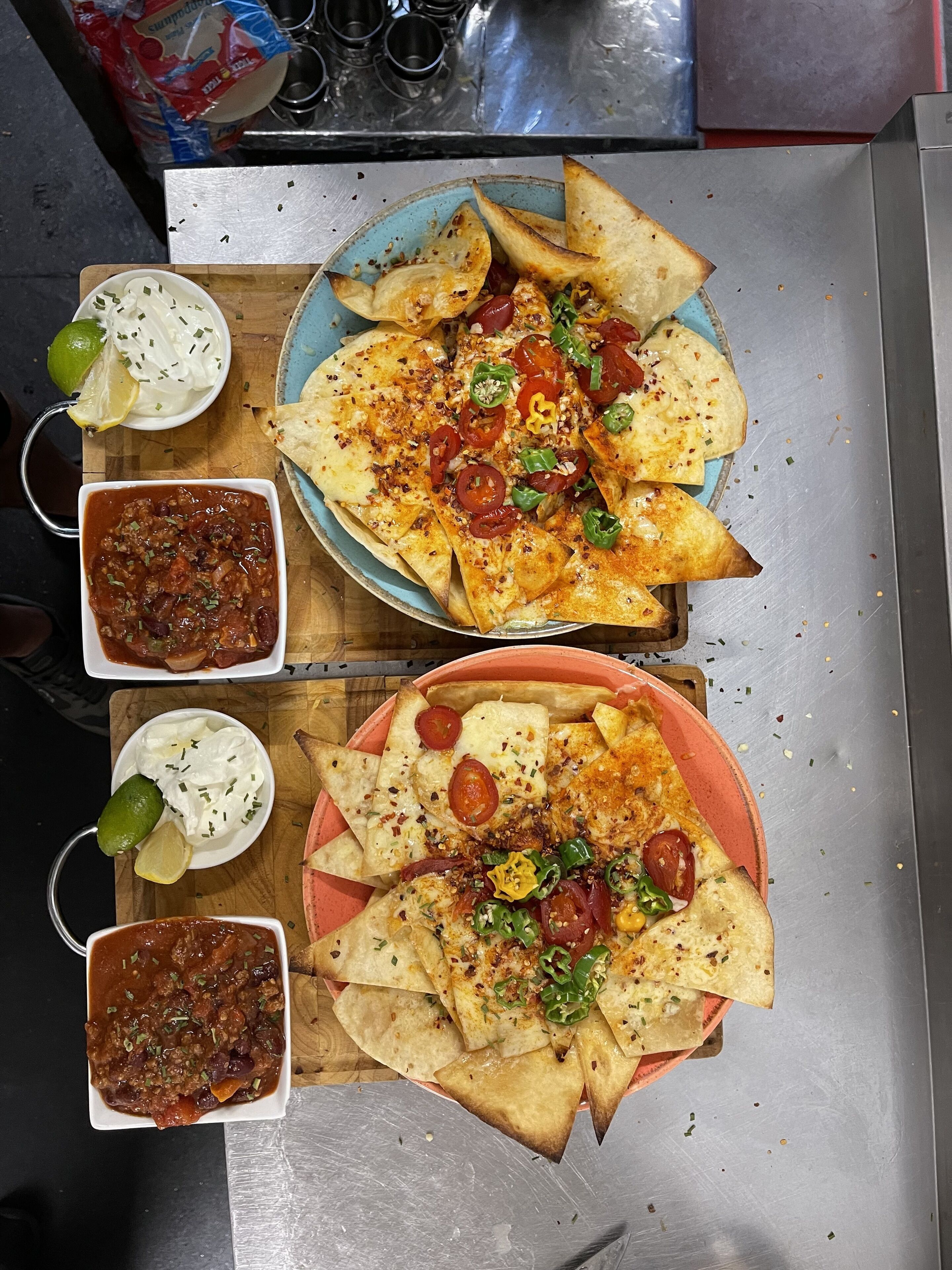 A meal consisting of nachos topped with cheese, tomatoes, and jalapeños, accompanied by two bowls of salsa and a lime wedge.