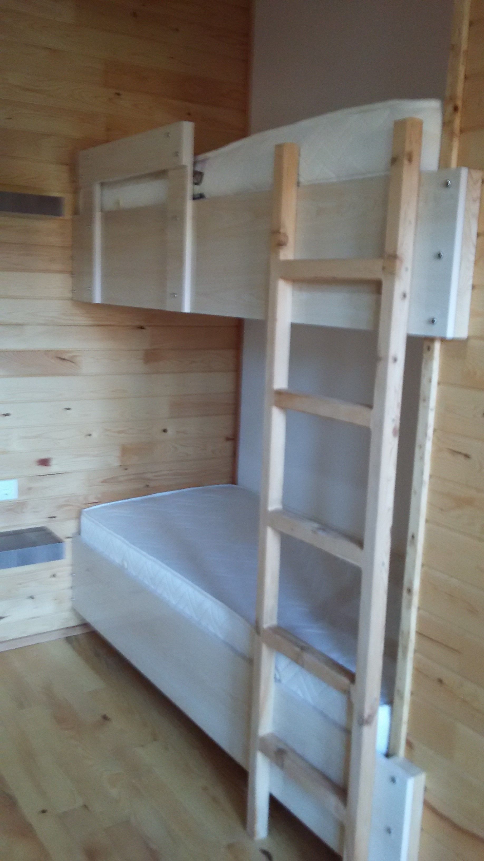 A bunk bed with a ladder attached to the side, wooden walls, and a mattress.