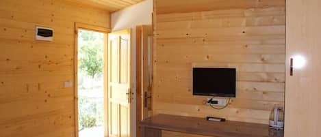 Un interior de madera con un televisor montado en la pared, una puerta que da al exterior y un mueble pequeño.