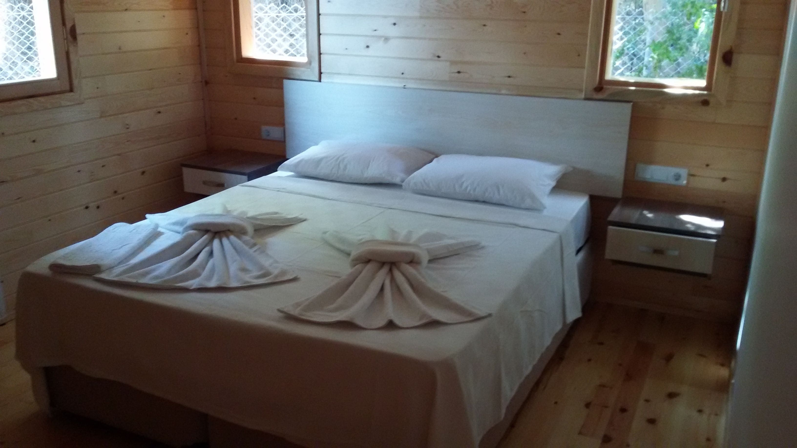 A wooden-paneled room with a bed, two nightstands, and a window.