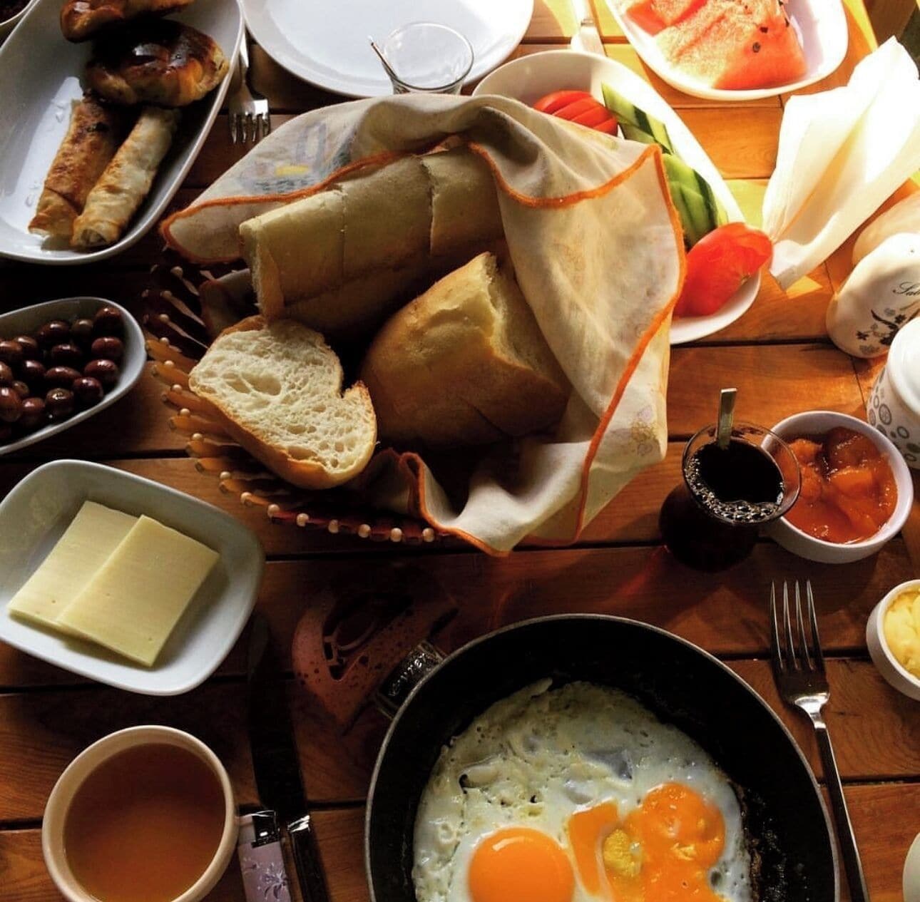 Une table en bois dressée pour le petit-déjeuner, avec des œufs, des toasts, des saucisses et divers accompagnements.