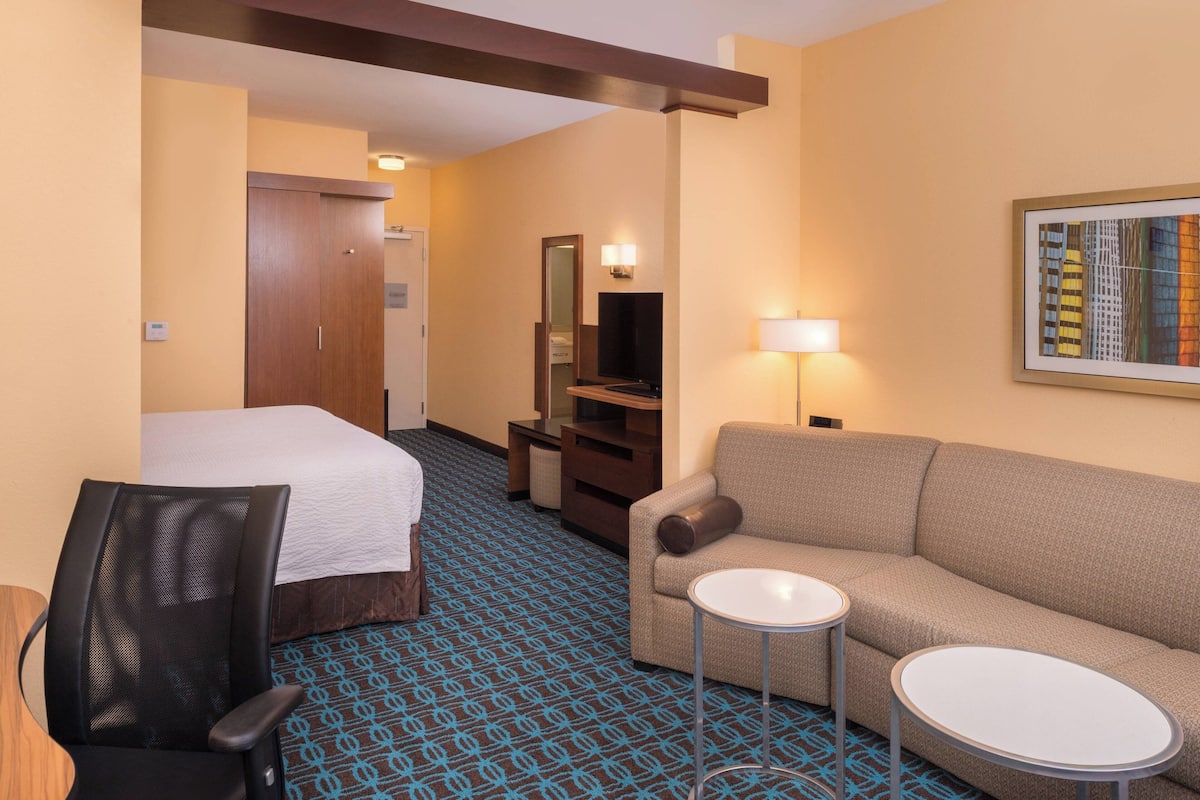 Ein Hotelzimmer mit Bett, Sofa, kleinem Tisch, Stuhl, Fernseher und Spiegel.