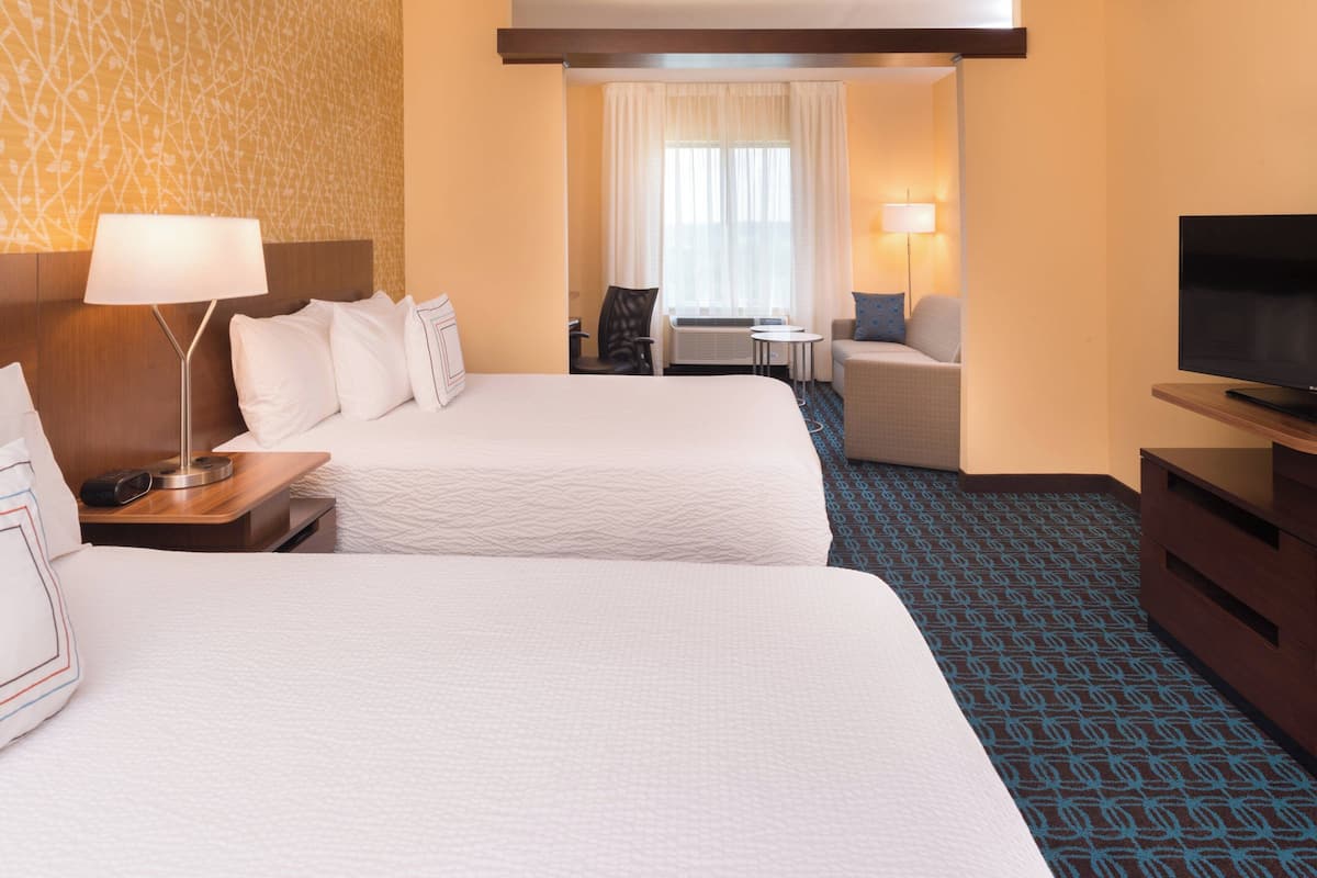 Ein Hotelzimmer mit zwei Betten, einem Fernseher, einem Schreibtisch mit Lampe, einem Sessel und einem kleinen Tisch.