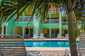 Une zone de piscine avec des chaises longues et, au fond, un bâtiment doté de balcons.