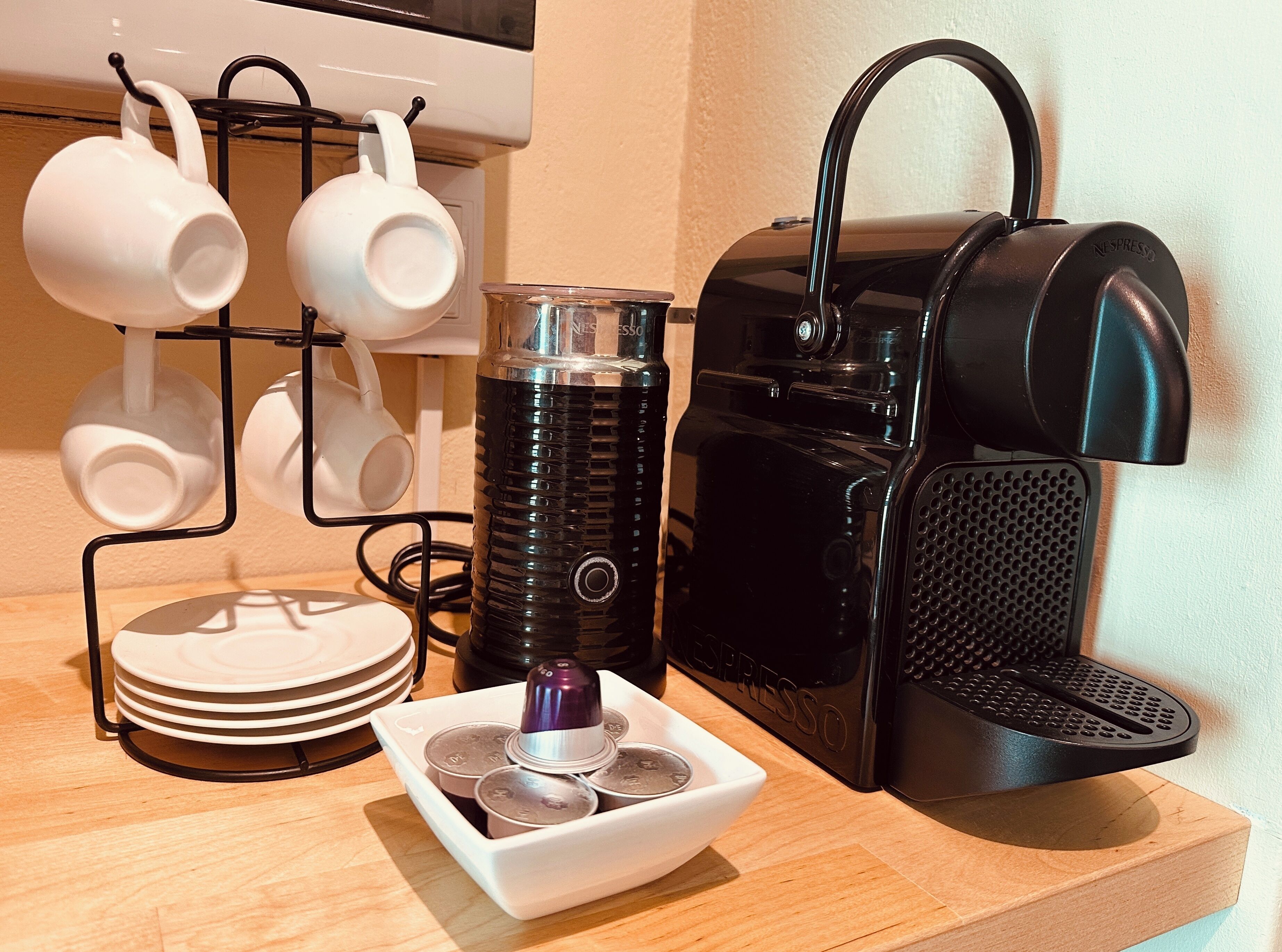 A coffee machine, a stack of plates, and a mug holder with cups on a wooden surface.