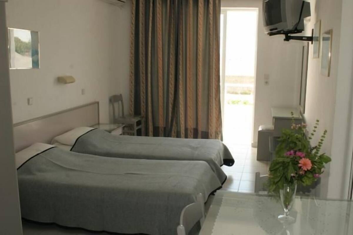 A hotel room with two beds, a desk, a chair, a TV mounted on the wall, and a window with curtains.